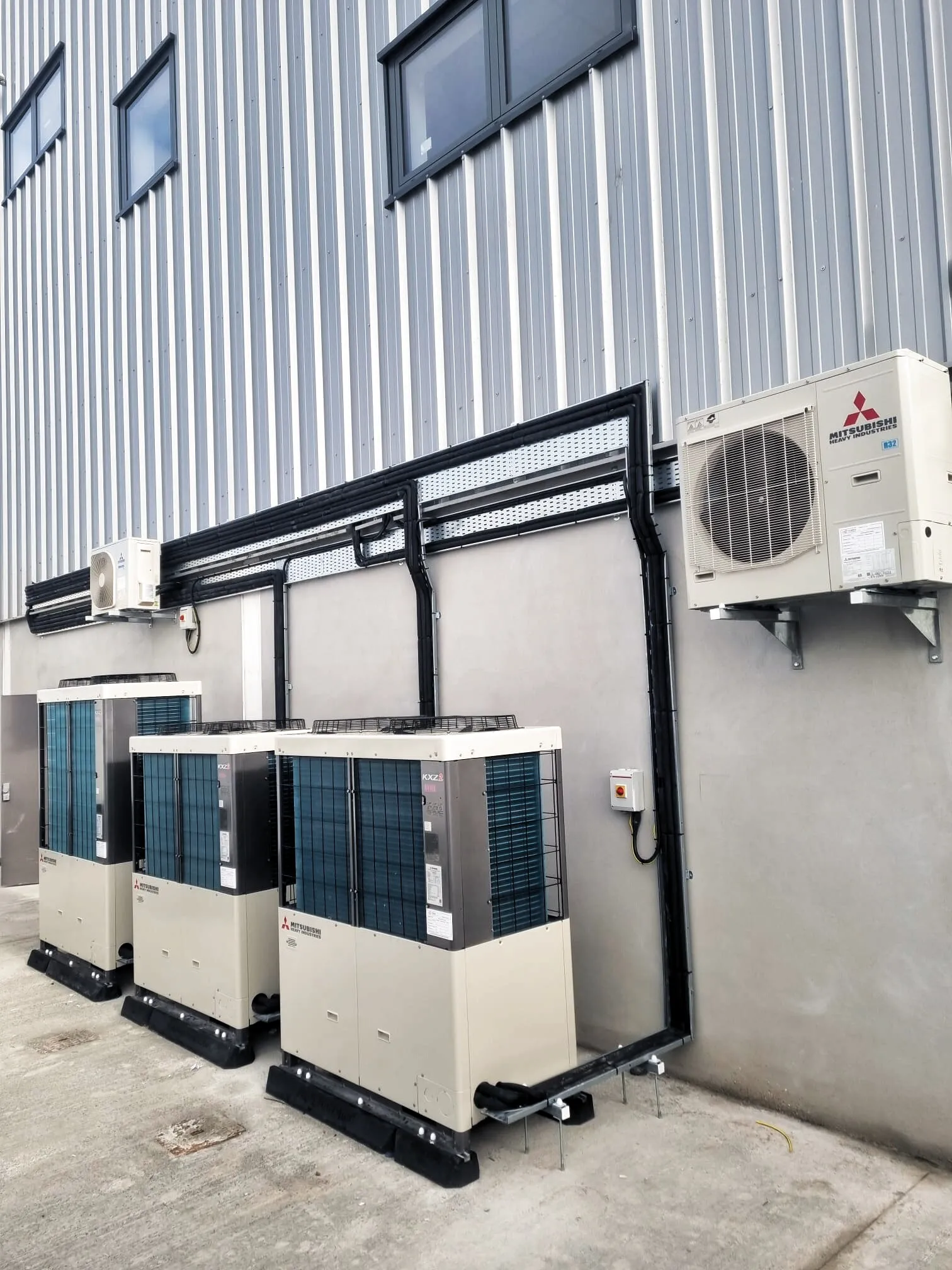 Mitsubishi VRF outdoor units with insulated pipework on a commercial wall